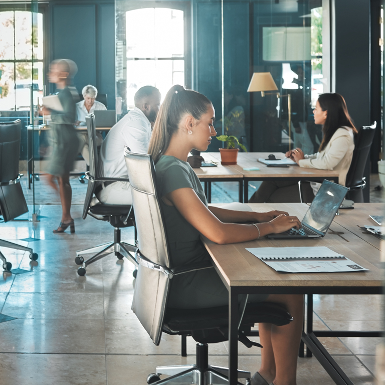 A diverse group of professionals working on laptops and collaborating in a bright, open-plan office, illustrating teamwork and proactive actions for cyber resilience