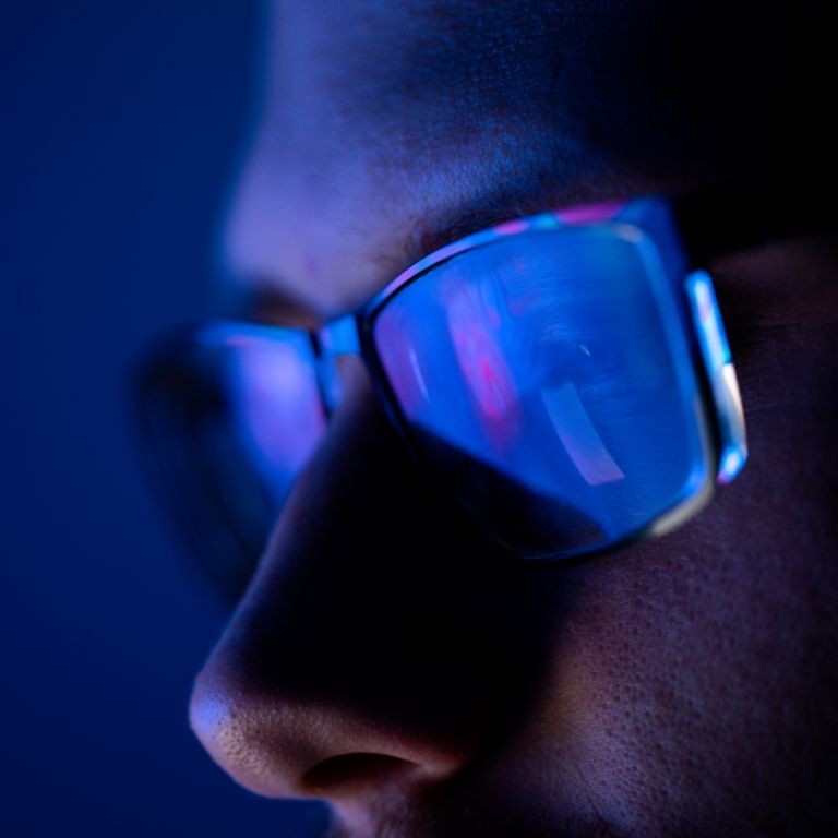 Cyber risk landscape concept—close-up of a person wearing glasses with a computer screen reflected in the lenses in low light.
