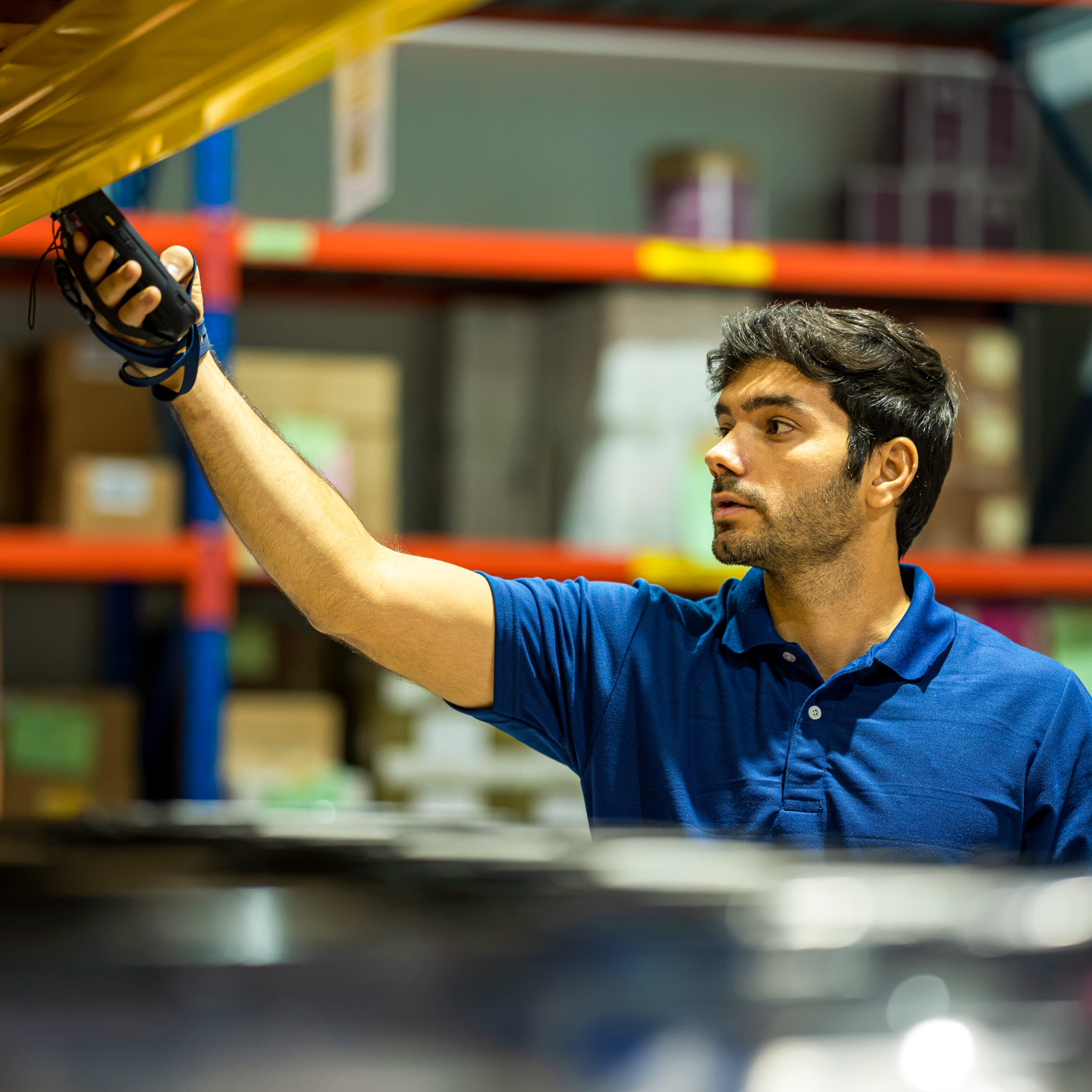 Warehouse employee reaching up to grab an item from industrial shelving in a busy stockroom, illustrating Employee rust-out and disengagement.