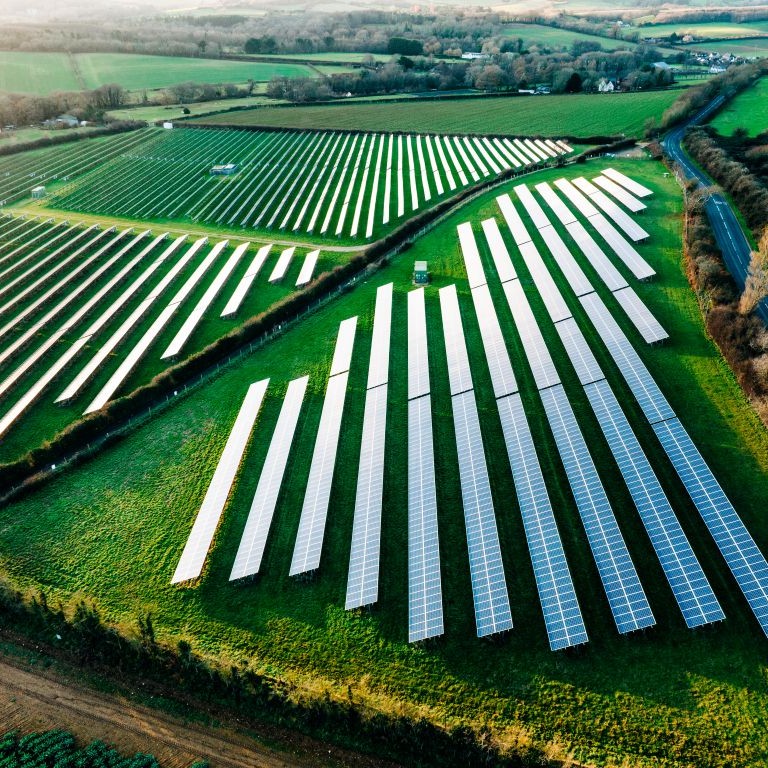 Large solar farm with long rows of photovoltaic panels on green farmland, relevant to insurance for renewable energy projects