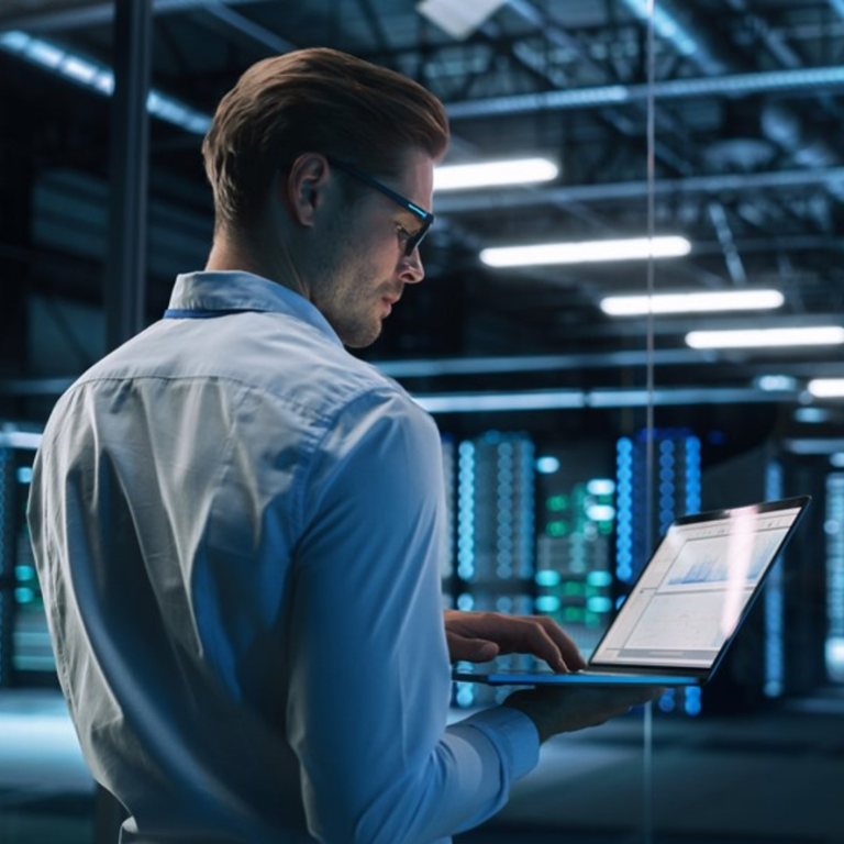 Professional in a white shirt using a laptop in a data centre, surrounded by server racks, analysing data related to cyber risk and cyber insurance.