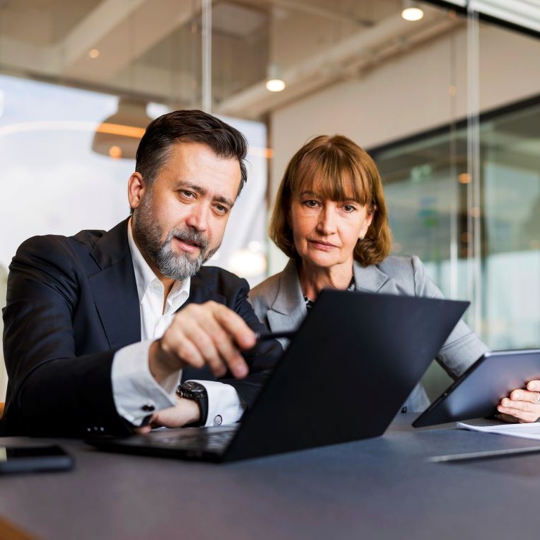 Two colleagues in a modern office review documents on a laptop and tablet during a cyber insurance review.