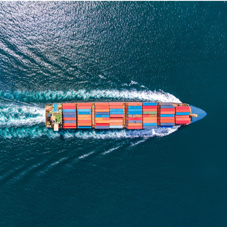 Aerial view of a large cargo ship filled with colourful containers, navigating through deep blue waters, illustrating the complexities of international trade and tariffs.