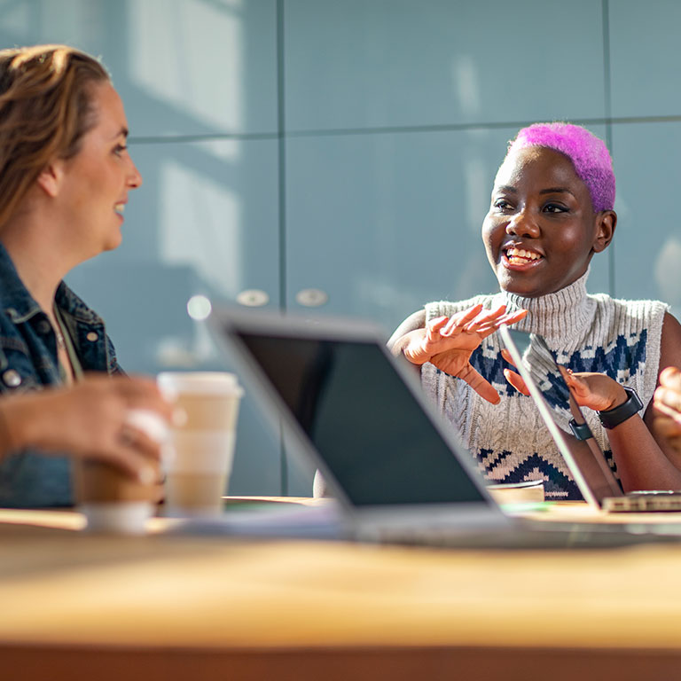 A diverse group of professionals engaged in a meeting around a table with laptops and coffee, collaborating on cyber risk management solutions
