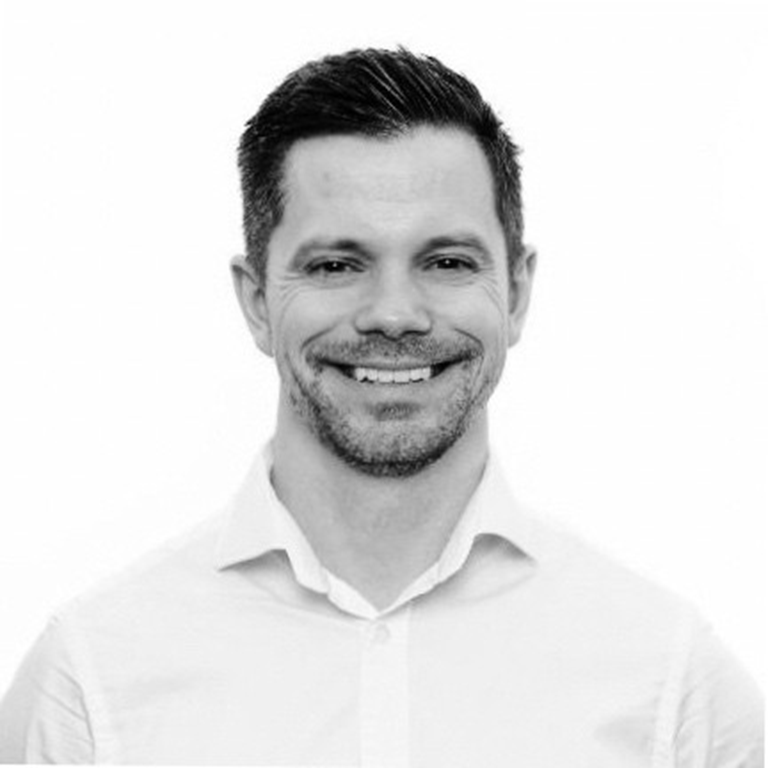 John Kavanagh in a white shirt smiling, standing against a plain background.
