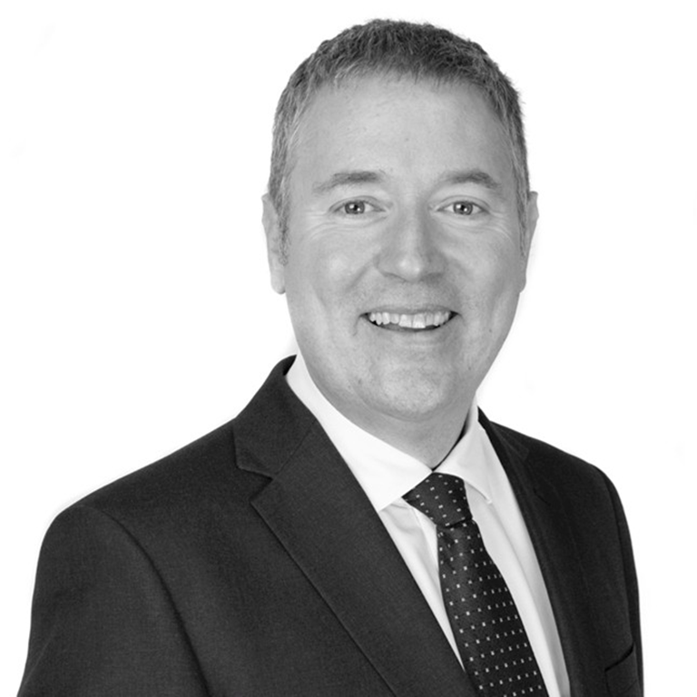 Jonathan Webb wearing a dark suit and dotted tie, posing against a white background.