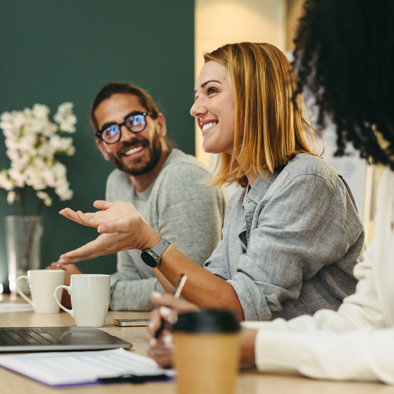 A group of retail employees engaged in a meeting, discussing strategies for improving employee wellbeing, with a laptop and coffee cups on the table.