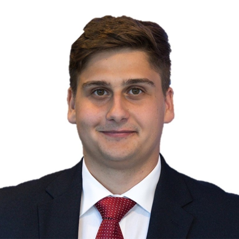 A man in a dark suit, white shirt, and red tie, posing against a plain white background.