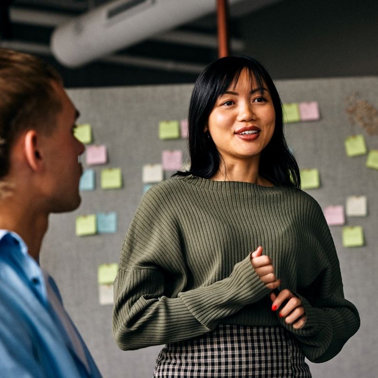 UK employment rights changes concept—woman speaking to colleagues during an office meeting with sticky notes on a wall behind her.