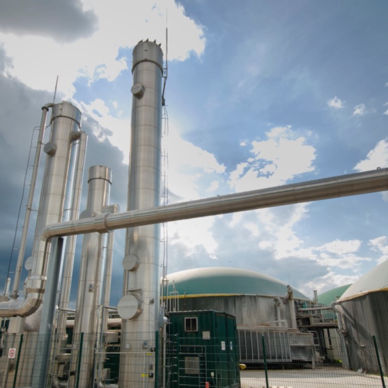 A modern anaerobic digestion plant with large domed digesters and tall metal pipes under a partly cloudy sky, showing the facility used for converting organic waste into renewable energy