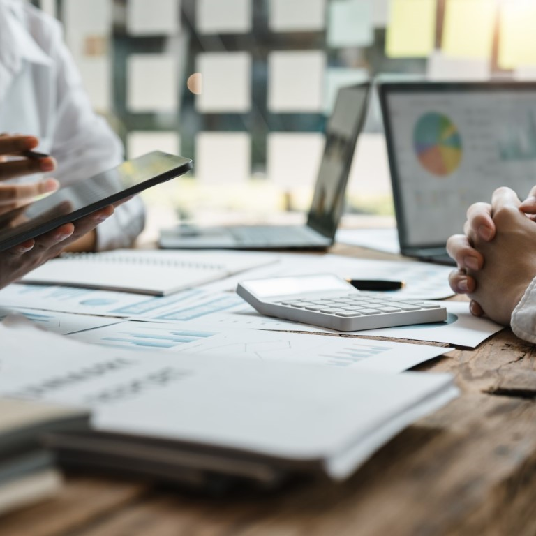 A group of professionals discussing claims and risk management strategies, with documents, a tablet, and a laptop on a wooden table, showcasing collaboration and analysis.