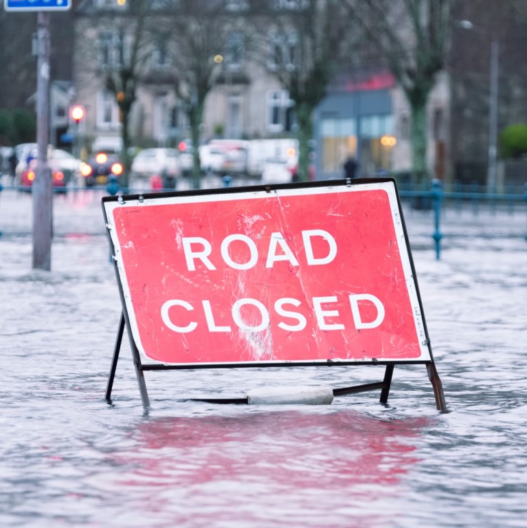 A flooded street with a "Road Closed" sign, highlighting the impact of storm damage on urban areas and the importance of insurance claims for recovery.